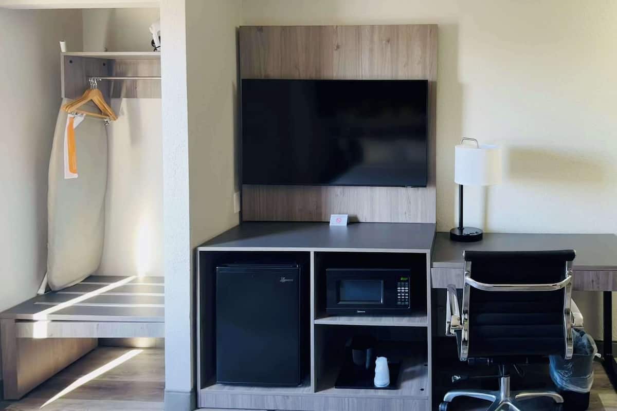 A compact hotel room with a flat-screen TV, a microwave, a mini-fridge, a chair, and a small table.