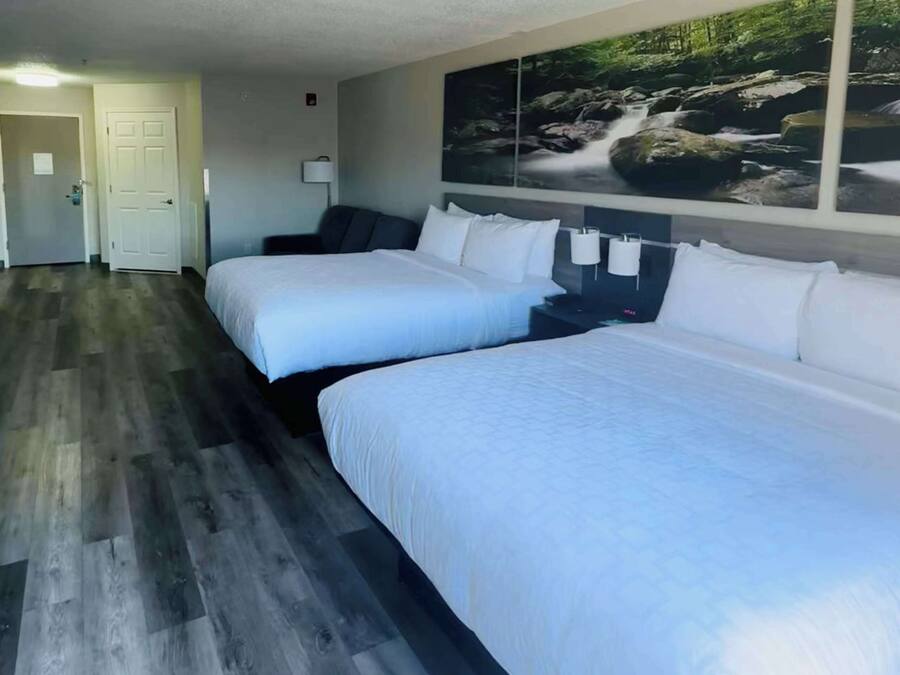 A hotel room with two beds, a wooden floor, a painting of a waterfall on the wall, and a door in the background.