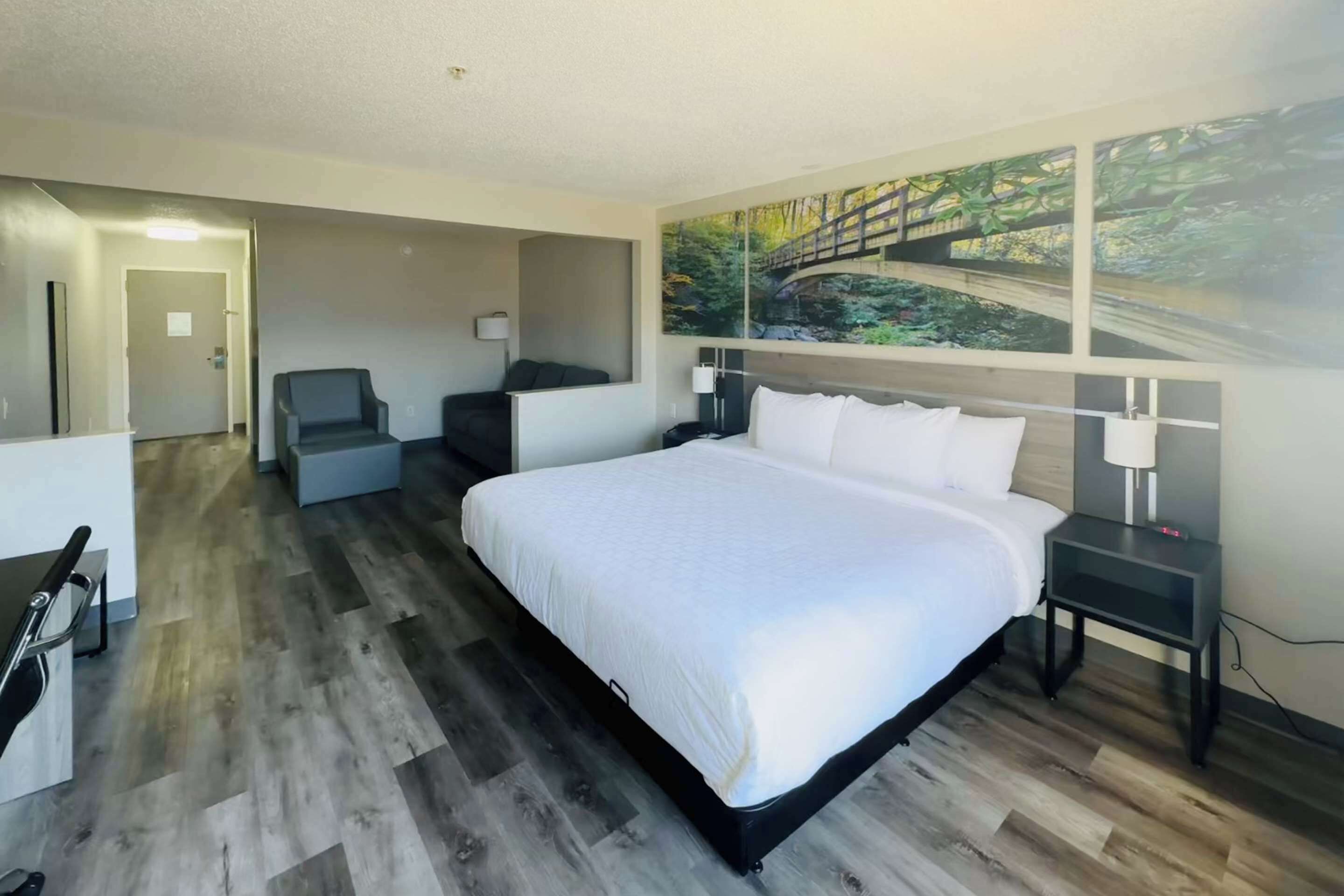 A modern hotel room with a large bed, a desk, a chair, and a painting of a bridge.