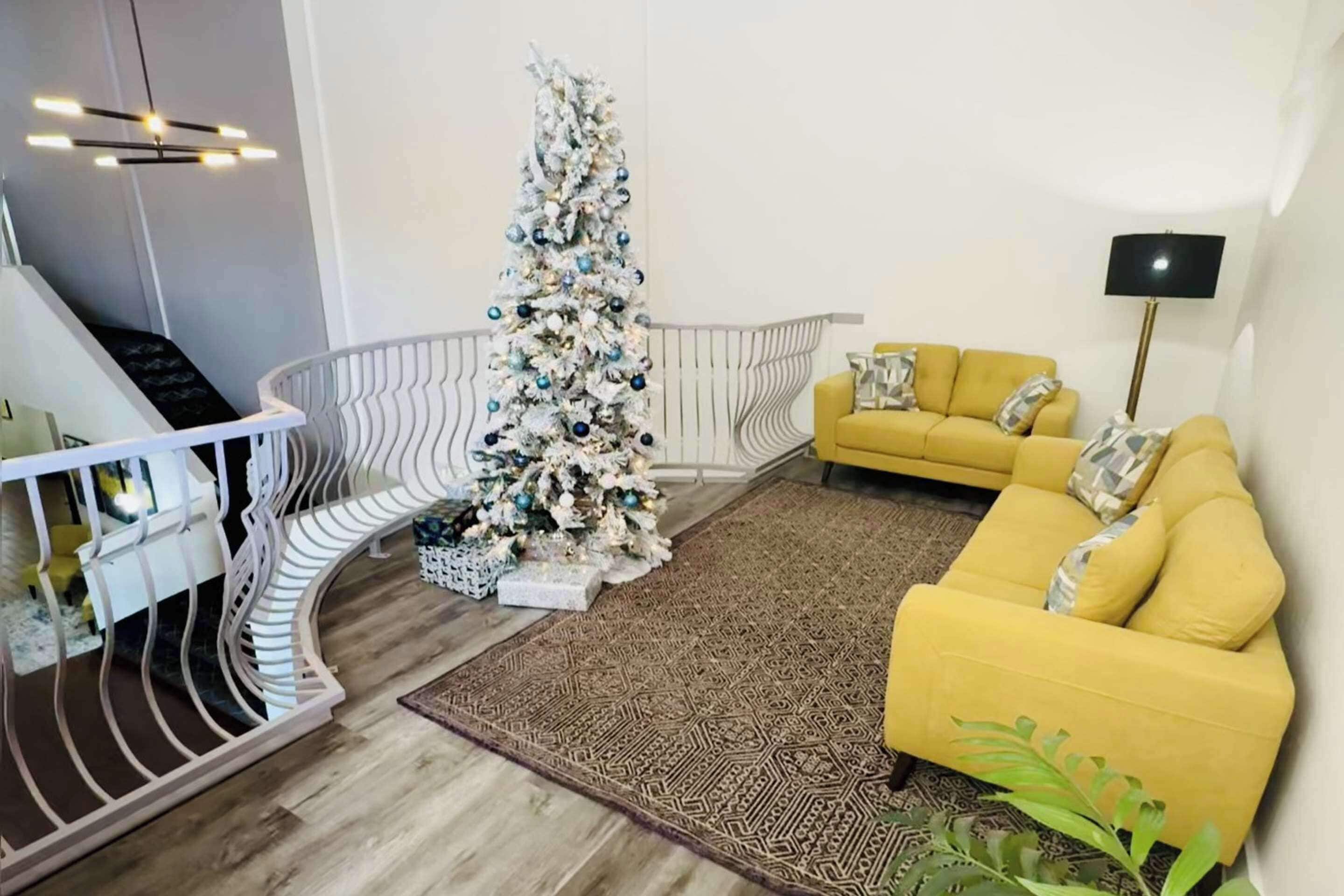 Un salon avec un canapé jaune, un escalier blanc et un sapin de Noël.