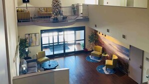 A spacious lobby with a high ceiling, a Christmas tree, and a balcony with seating. - Clarion Pointe Albemarle (Albemarle)