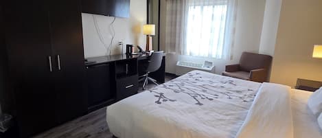 Quarto de hotel com uma cama grande, uma escrivaninha, uma cadeira, um guarda-roupa e uma televisão.