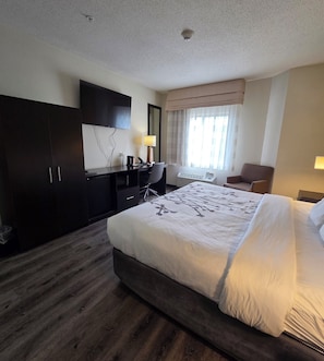 A hotel room with a large bed, a desk, a chair, a wardrobe, and a television. - Austinburg Hotel (Austinburg)
