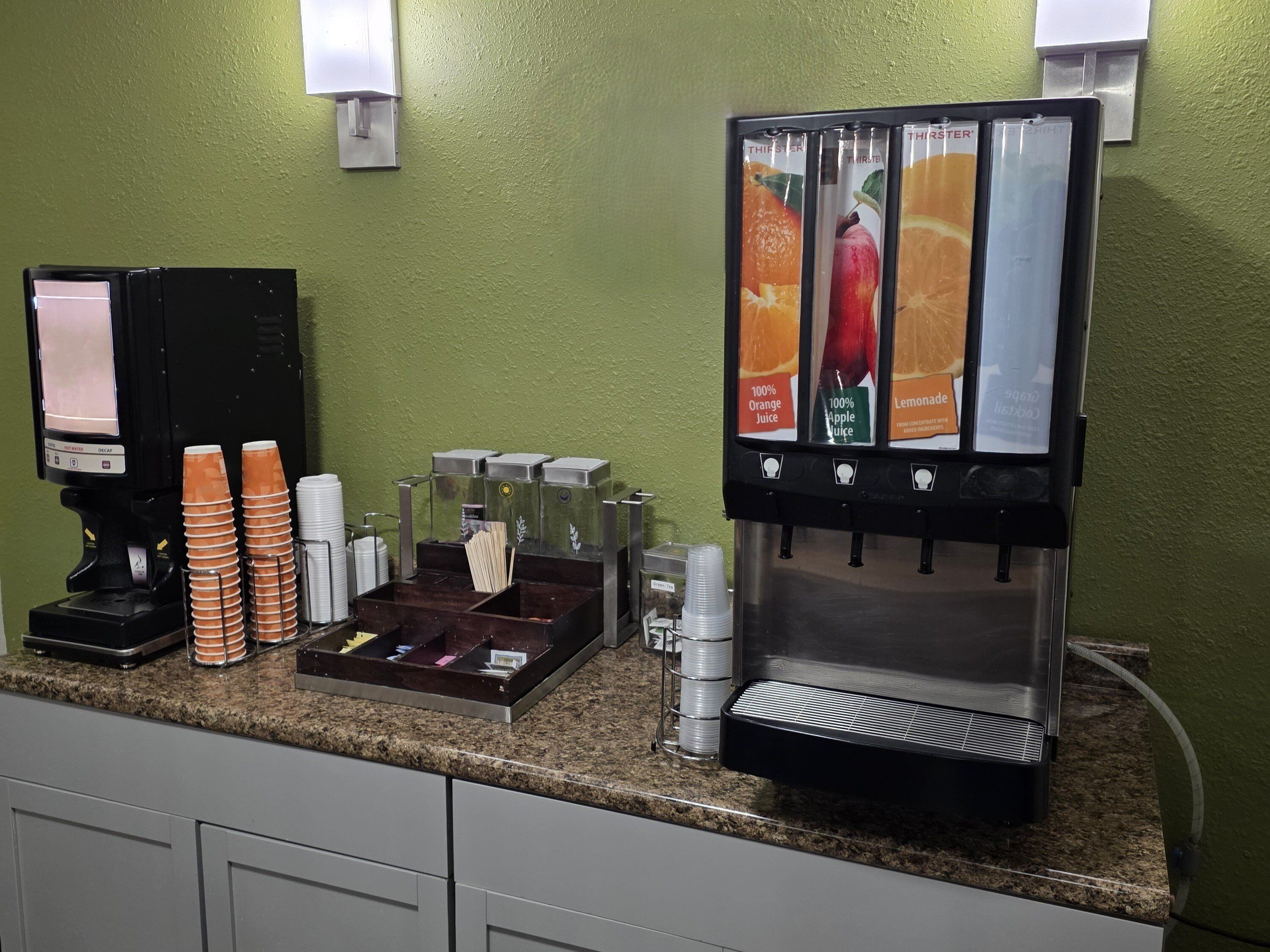 A coffee station with a beverage dispenser, a coffee machine, and a stack of disposable cups.