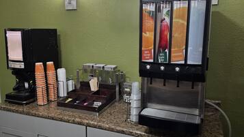 A coffee station with a beverage dispenser, a coffee machine, and a stack of disposable cups.