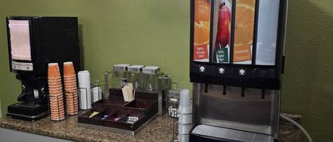 A coffee station with a beverage dispenser, a coffee machine, and a stack of disposable cups.