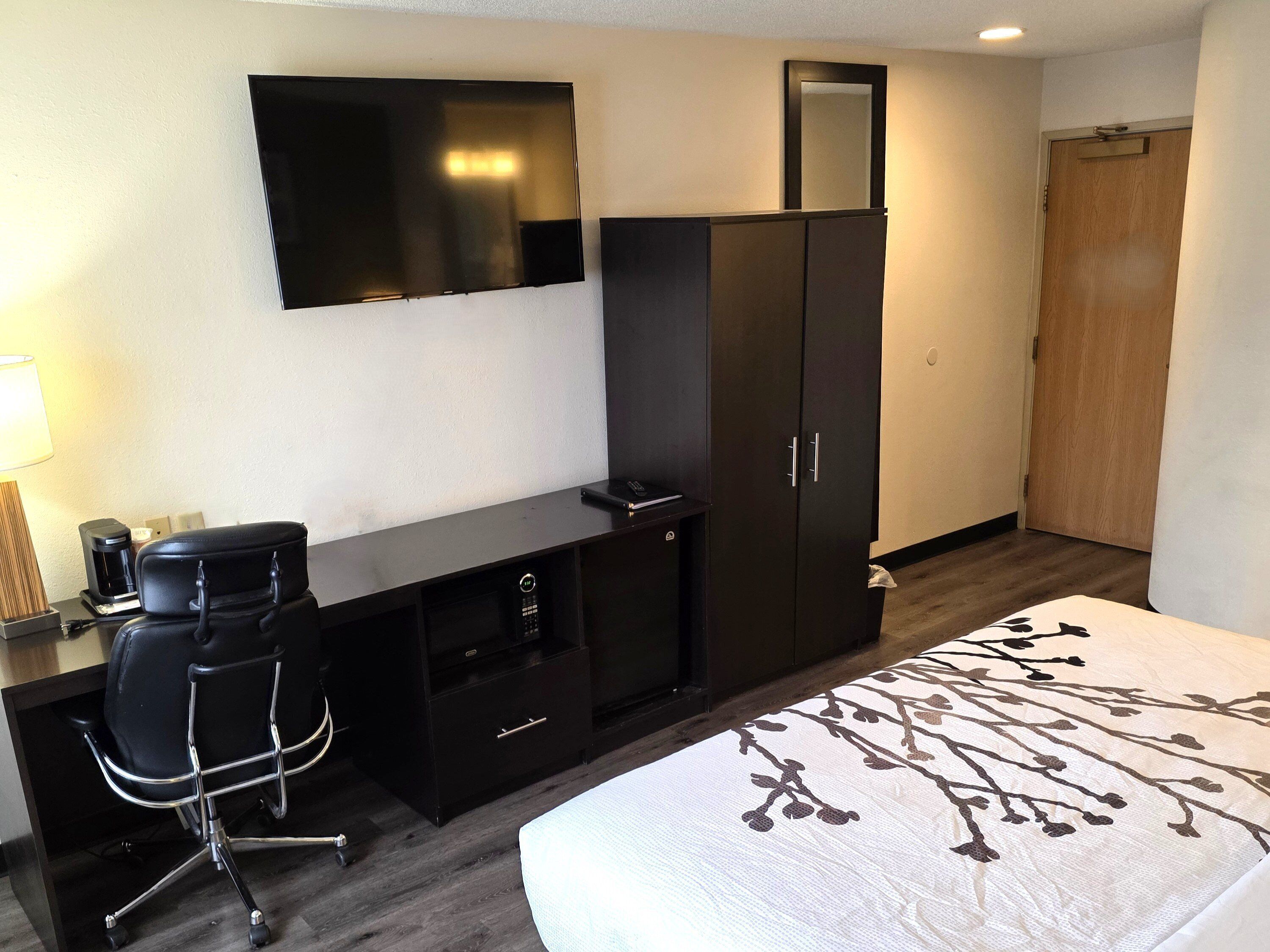 A hotel room with a bed, a desk with a chair, a wardrobe, a television, and a mirror.