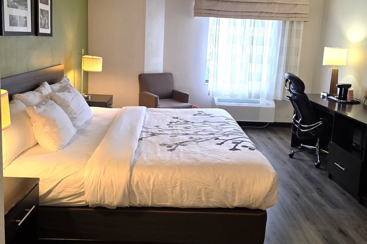 A hotel room with a bed, a desk, a chair, and a window with curtains.