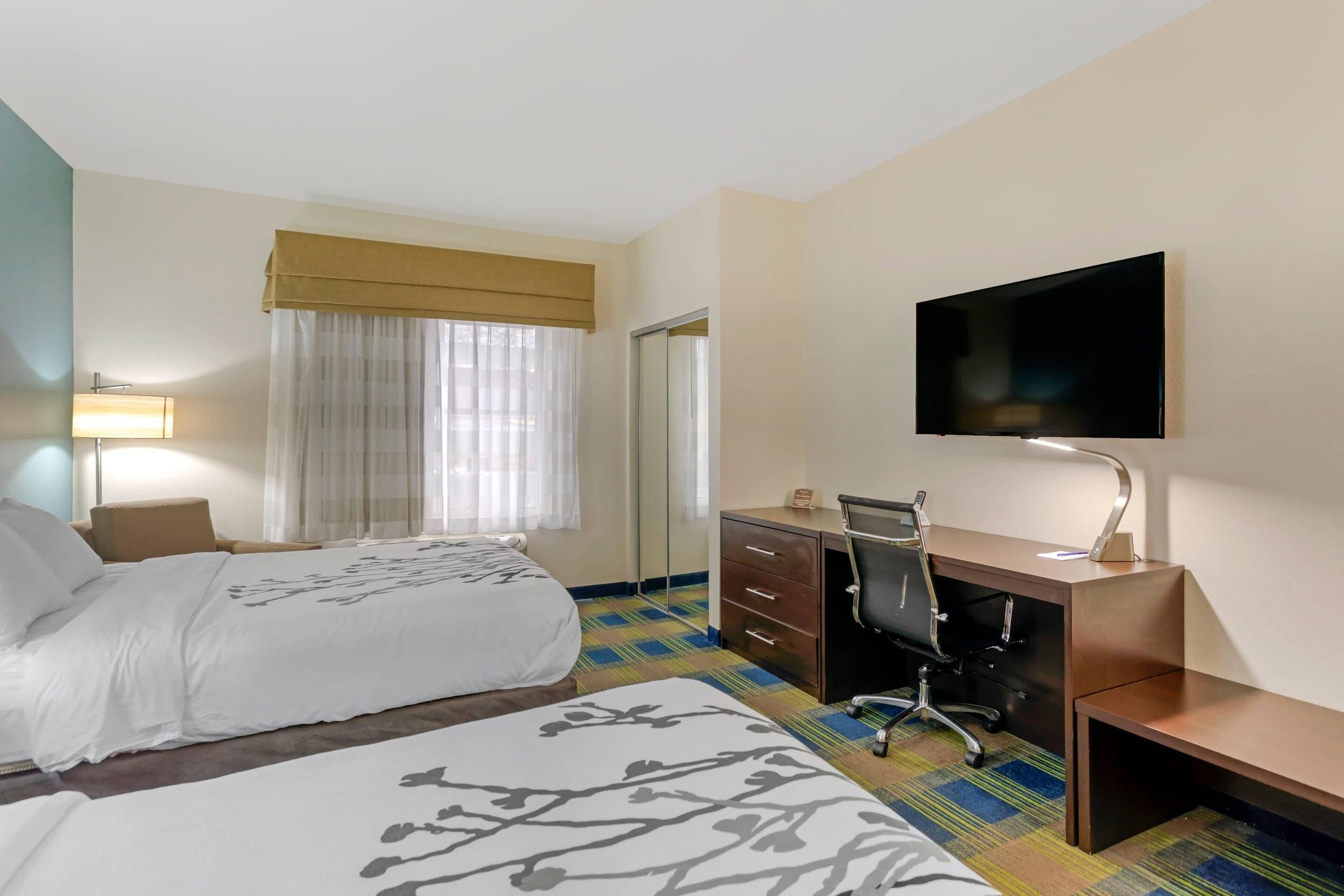 A hotel room with two beds, a desk, a chair, a television, and a window with curtains.