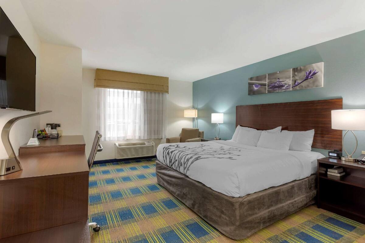 A hotel room with a bed, desk, and two bedside lamps.