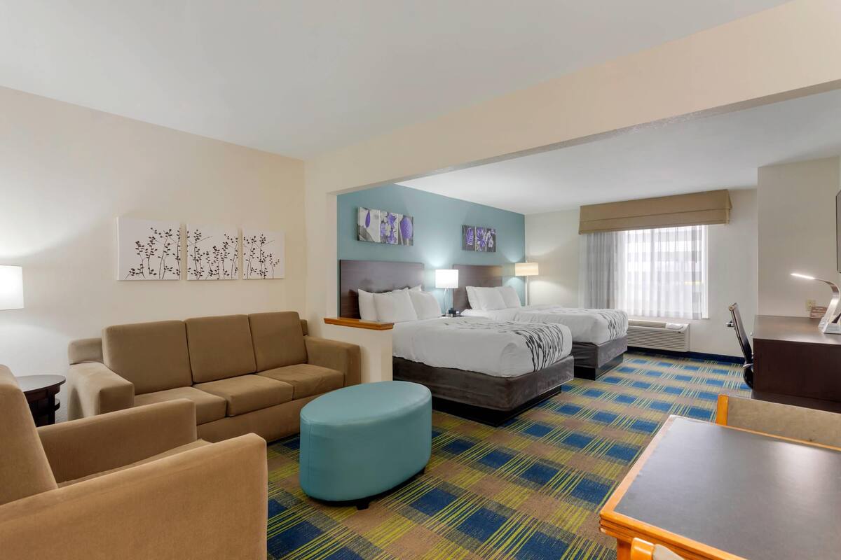 A hotel room with a sofa, ottoman, bed, and a small table.