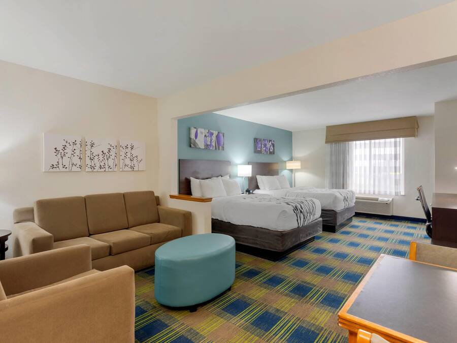 Habitación de hotel con sofá, reposapiés, cama y una pequeña mesa.