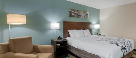 Habitación de hotel con cama, dos lámparas de noche, una mesita de noche, un sofá y una obra de arte en la pared.