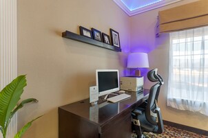 A hotel room with a desk, computer, chair, lamp, and framed pictures on the wall.