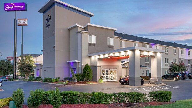 A modern hotel with a prominent entrance, a parking lot, and a sign for 'Sleep Inn & Suites by Crossroads Hotels'.