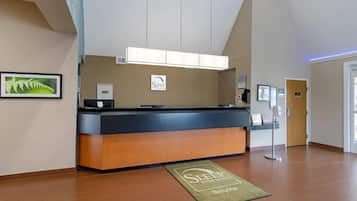 Un comptoir d’accueil avec une enseigne indiquant « Sleep Inn Suites », une fougère encadrée accrochée au mur et un tapis vert portant le nom de l’hôtel.