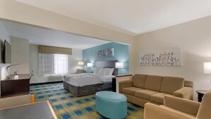 A hotel room with a bed, a sofa, a small table, a desk, and a TV.