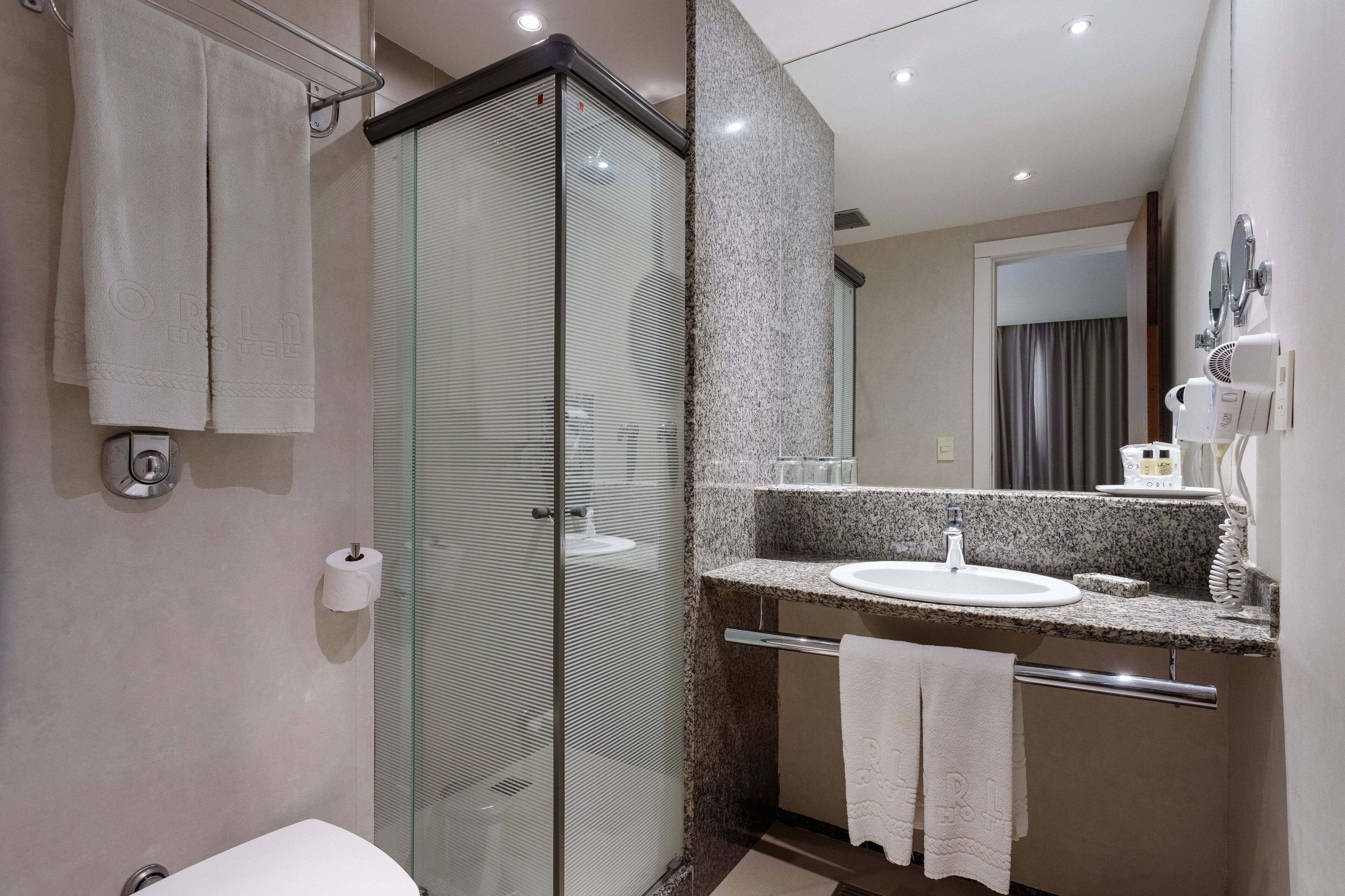 Une salle de bain moderne dotée d’une douche à parois de verre, d’un lavabo avec un plan de toilette en granit et d’un miroir agrémenté d’une coiffeuse.