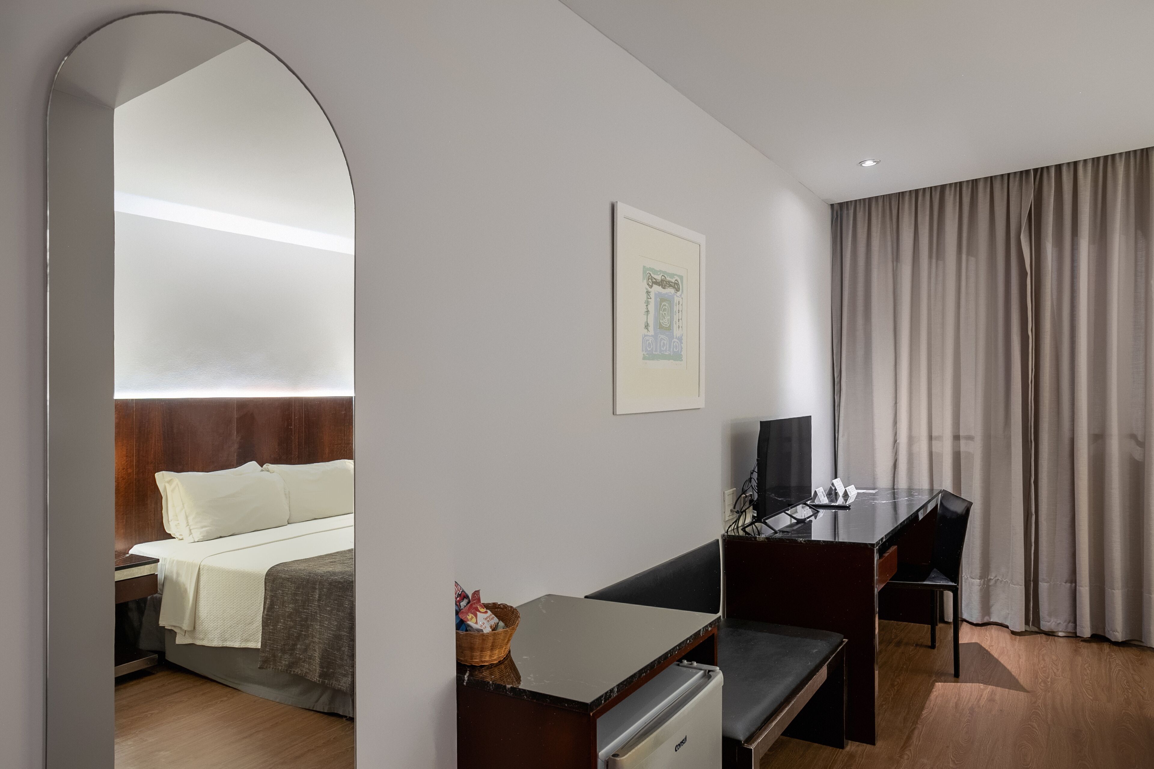 A hotel room with a bed, a desk, a chair, a television, and a window with curtains.