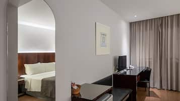 Ein Hotelzimmer mit Bett, Schreibtisch, Stuhl, Fernseher und einem Fenster mit Vorhängen.