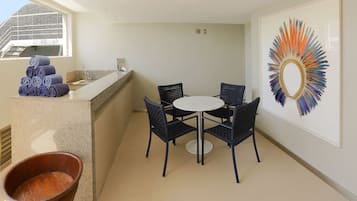 A sunlit room with a round table and chairs, a large window, and a wall-mounted artwork.