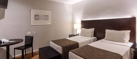 Habitación de hotel con dos camas, una mesita, una silla y un televisor.