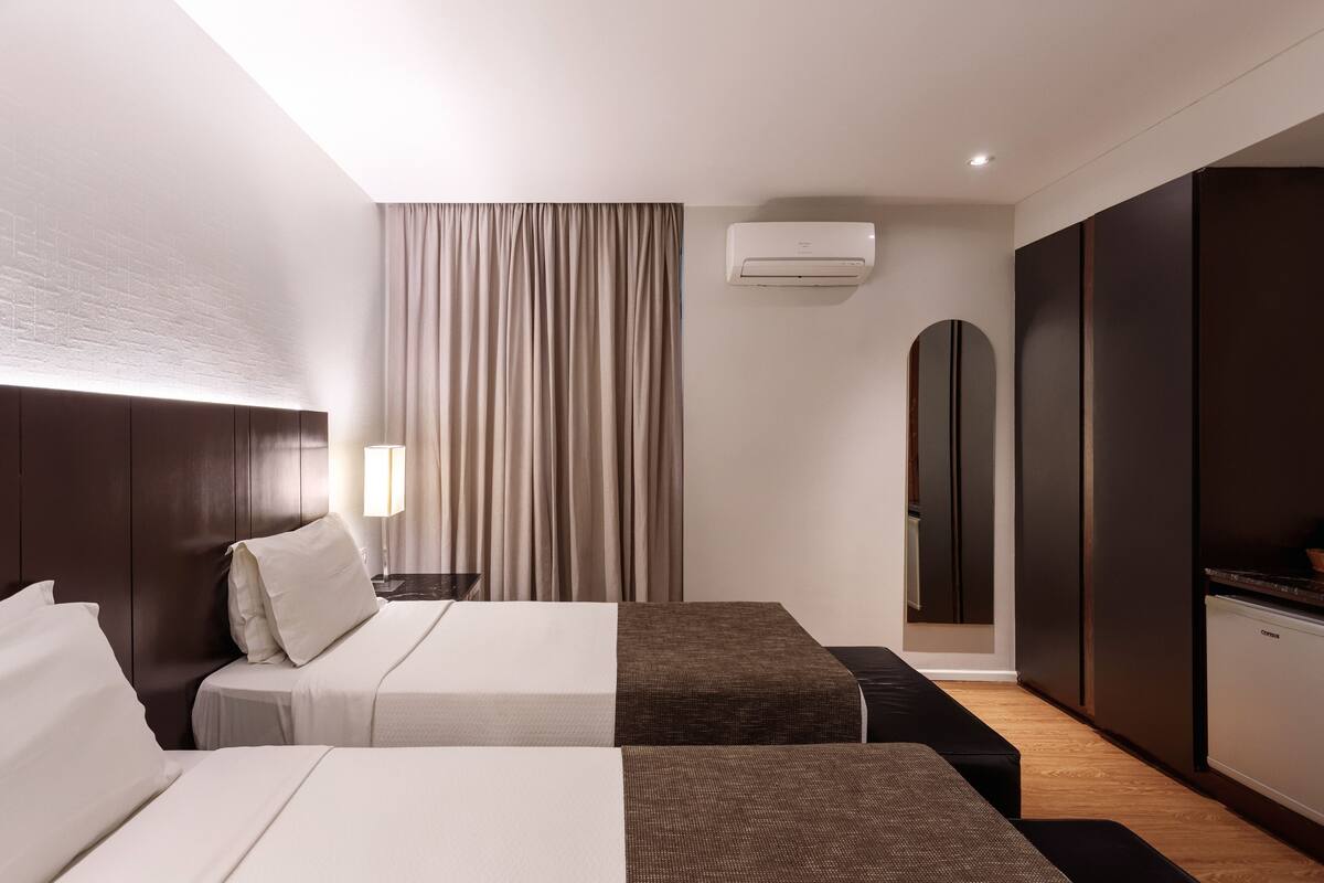 Hotelkamer met twee bedden, een bureau, een lamp, een airconditioner, een spiegel en een kledingkast.