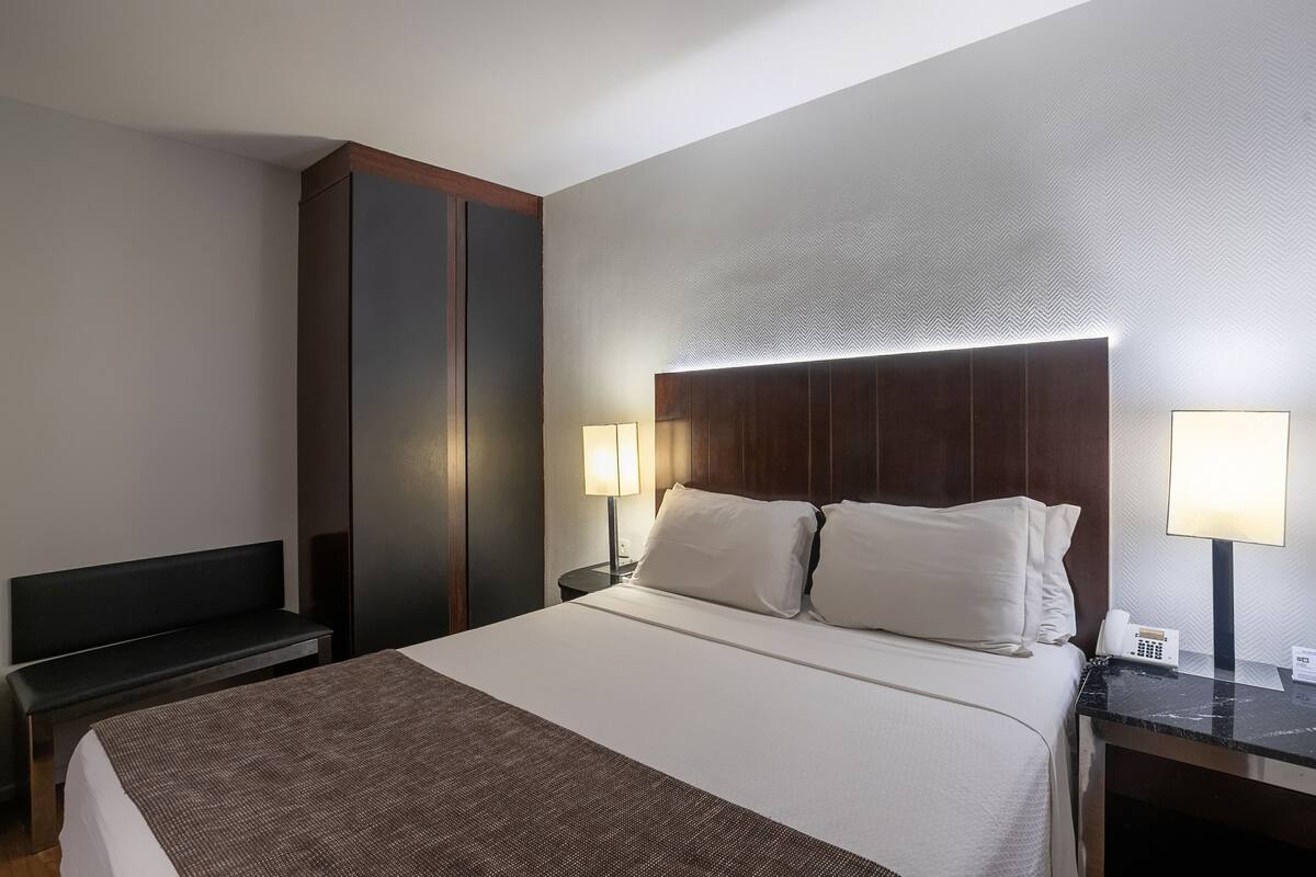 Een hotelkamer met een groot bed, twee bedlampen, een bureau en een kledingkast.