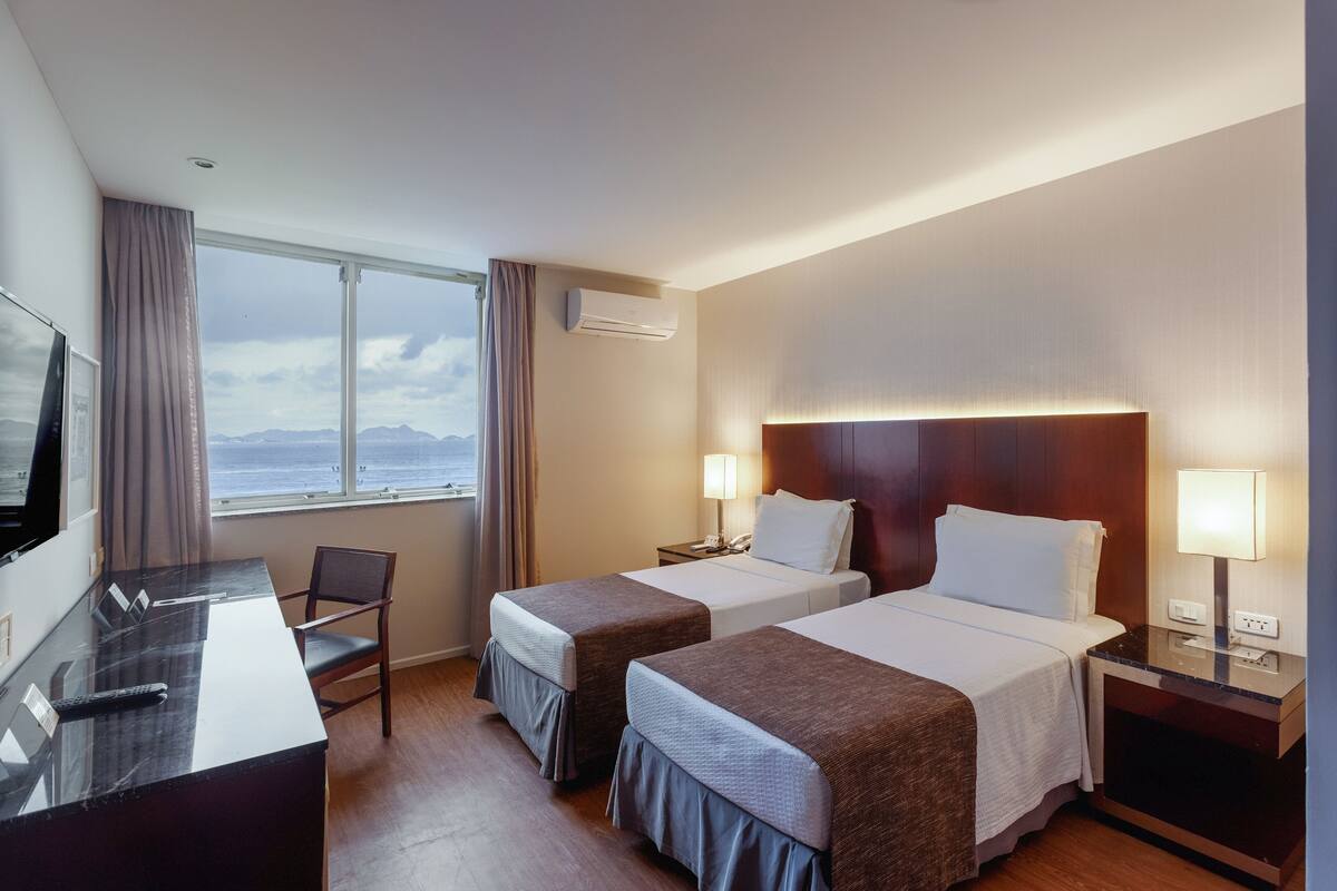 Hotelkamer met twee bedden, een bureau, een televisie en een raam met uitzicht op zee.