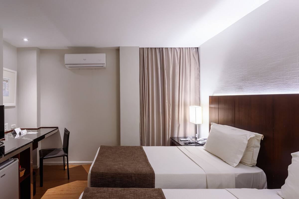 Een hotelkamer met een bed, een bureau, een stoel, een lamp en een airconditioning.