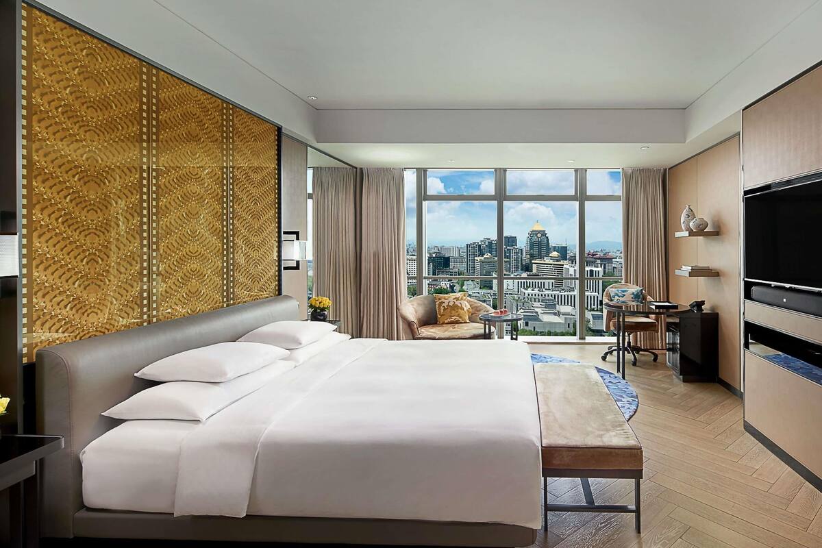 Habitación de hotel con cama, escritorio, televisor y vista a la ciudad.
