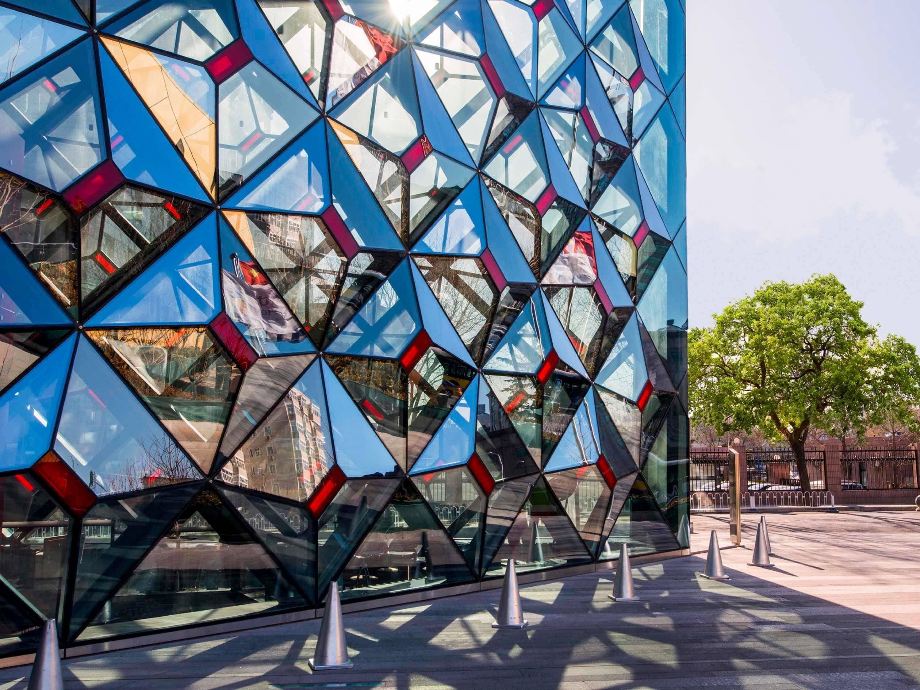 A modern building with a geometric glass facade and a tree in the background.