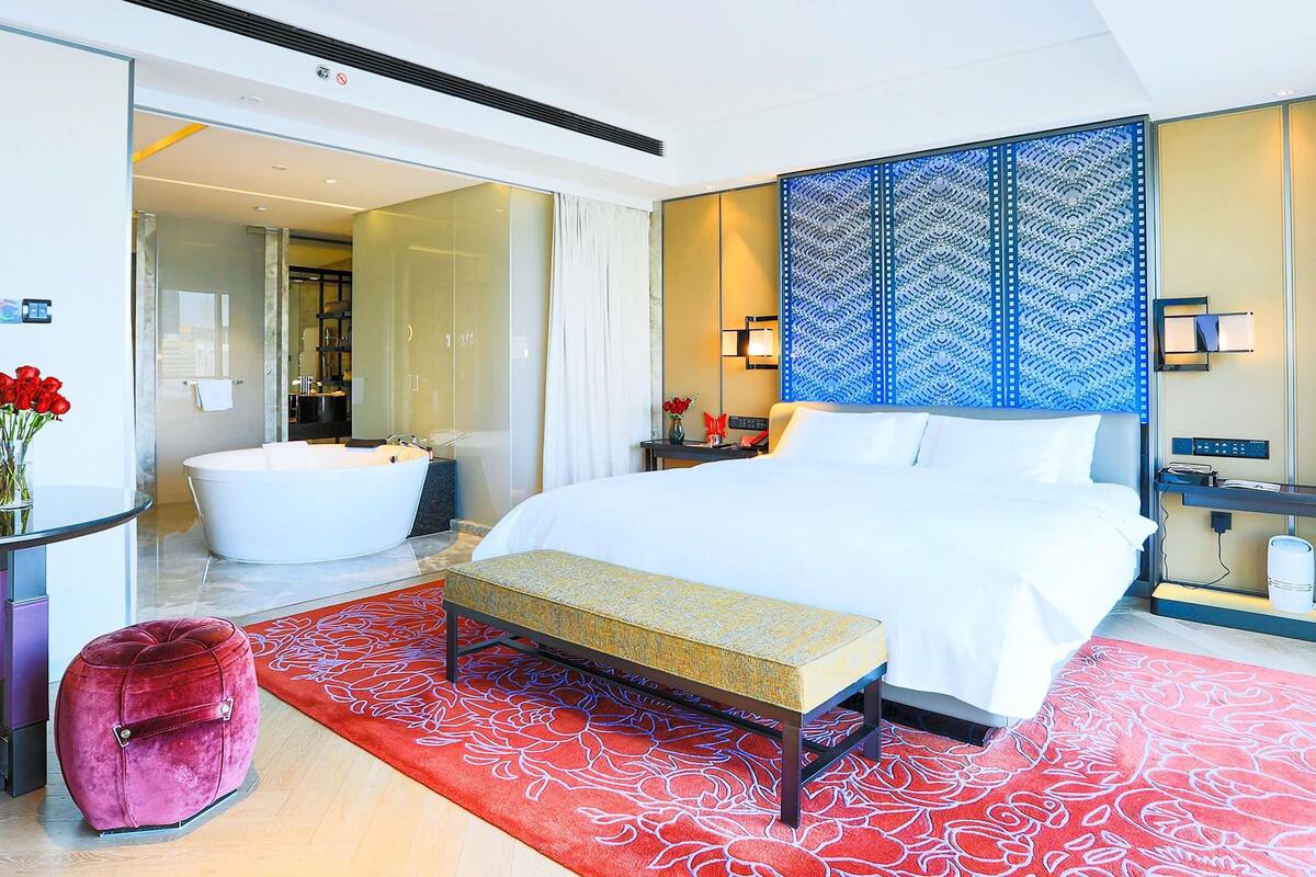 Una habitación de hotel moderna con una cama grande, una zona de estar, una bañera y un baño visible a través de una puerta abierta.