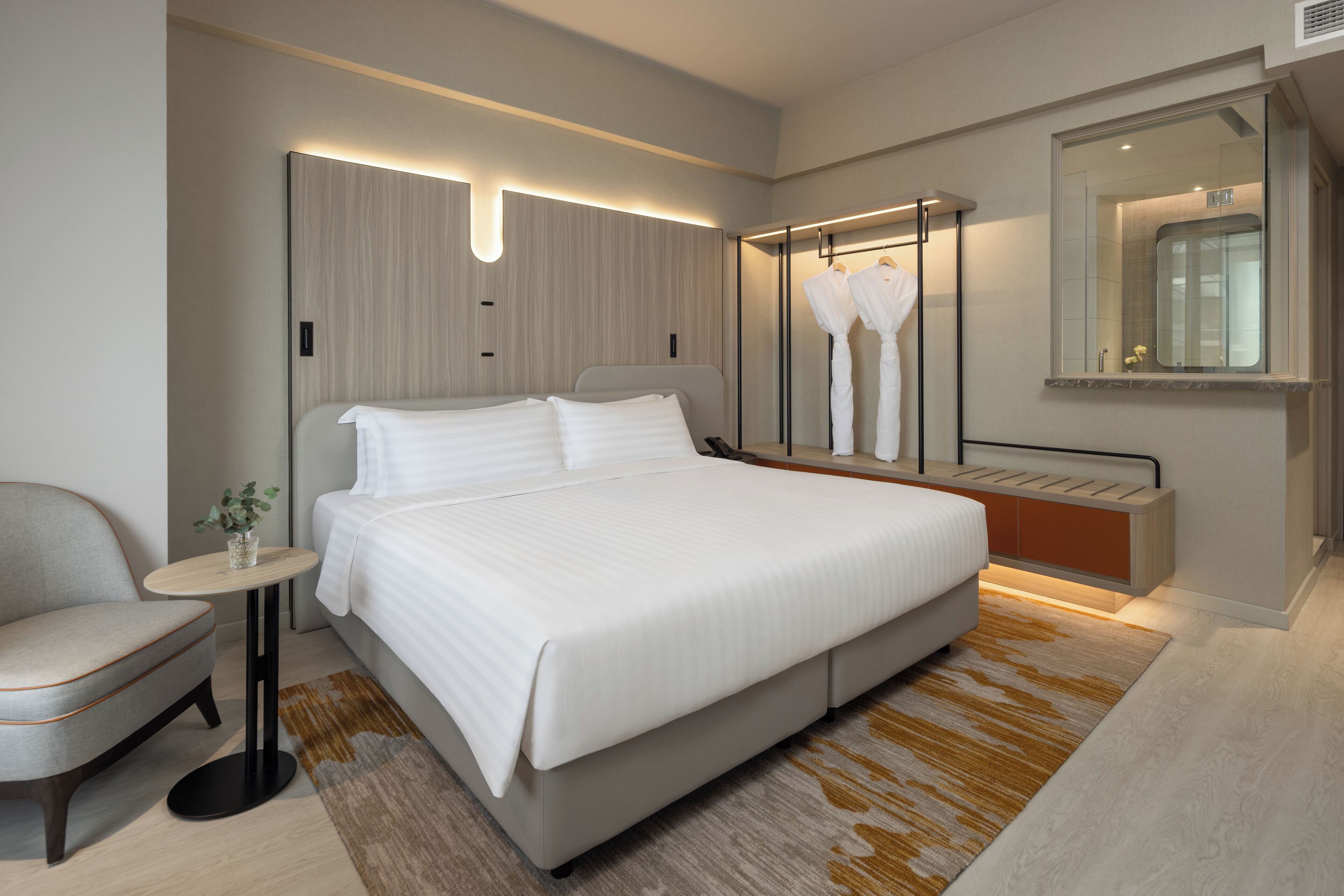 Une chambre d’hôtel moderne avec un grand lit, une table de chevet, une chaise et un miroir.