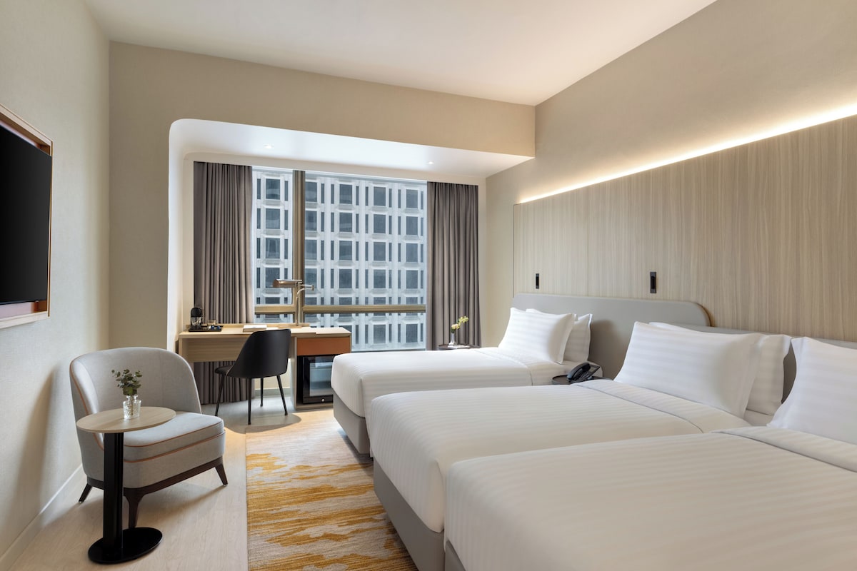 A hotel room with two beds, a desk, a chair, and a large window with curtains.