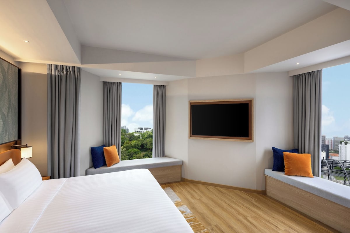 A hotel room with a large bed, a seating area with cushions, a view of the city, and a mounted television.