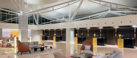 A spacious lobby with modern furniture, a high ceiling with structural beams, and a reception desk.