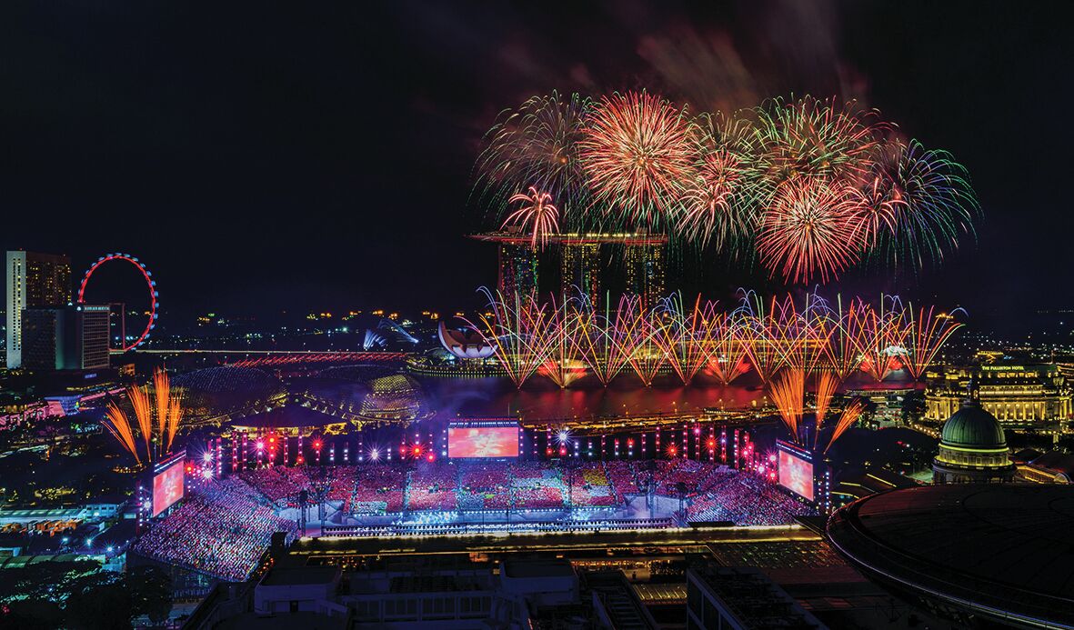 A nighttime cityscape with fireworks, a Ferris wheel, and illuminated buildings.