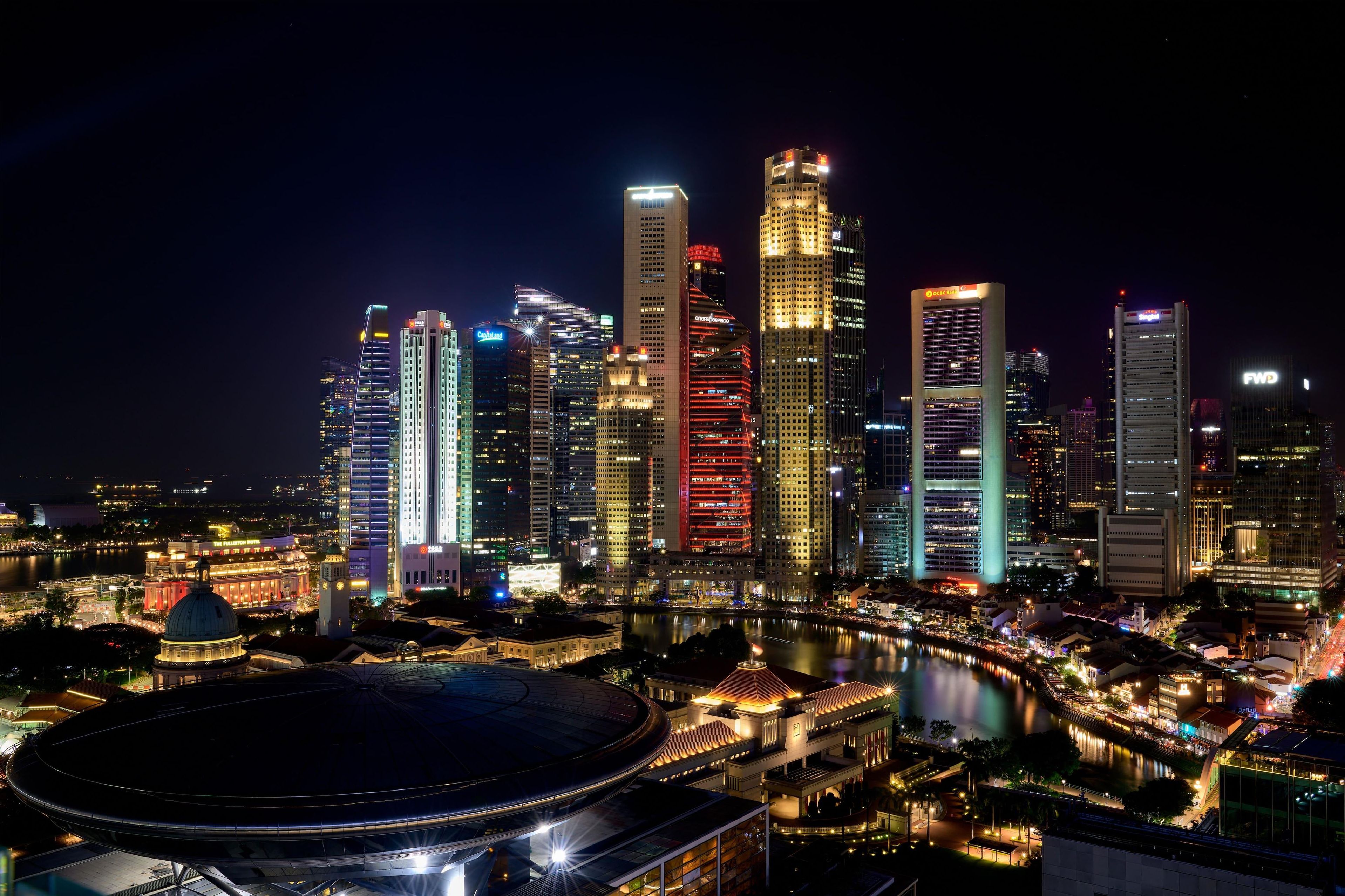 A nighttime cityscape with illuminated skyscrapers and a large stadium.