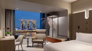 A modern hotel room with a large bed, a desk, a chair, and a view of a cityscape at night. - Wyndham Singapore Hotel (Singapore)