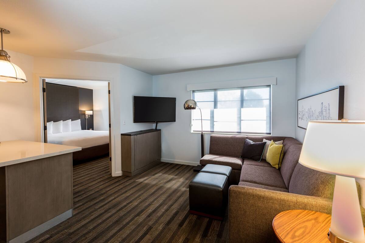 A hotel room with a bed, a TV, a sofa, a desk, and a window.