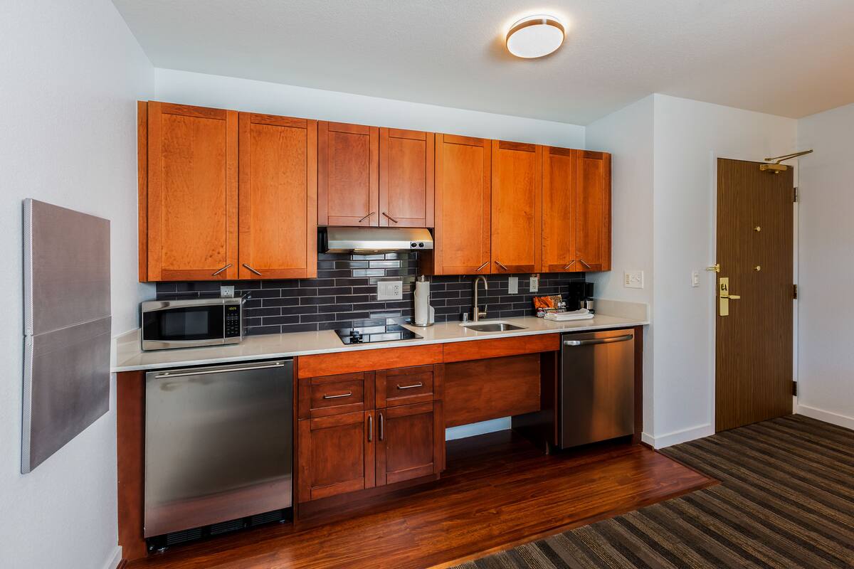 A compact kitchen with wooden cabinets, a stainless steel refrigerator, a microwave, and a dishwasher.
