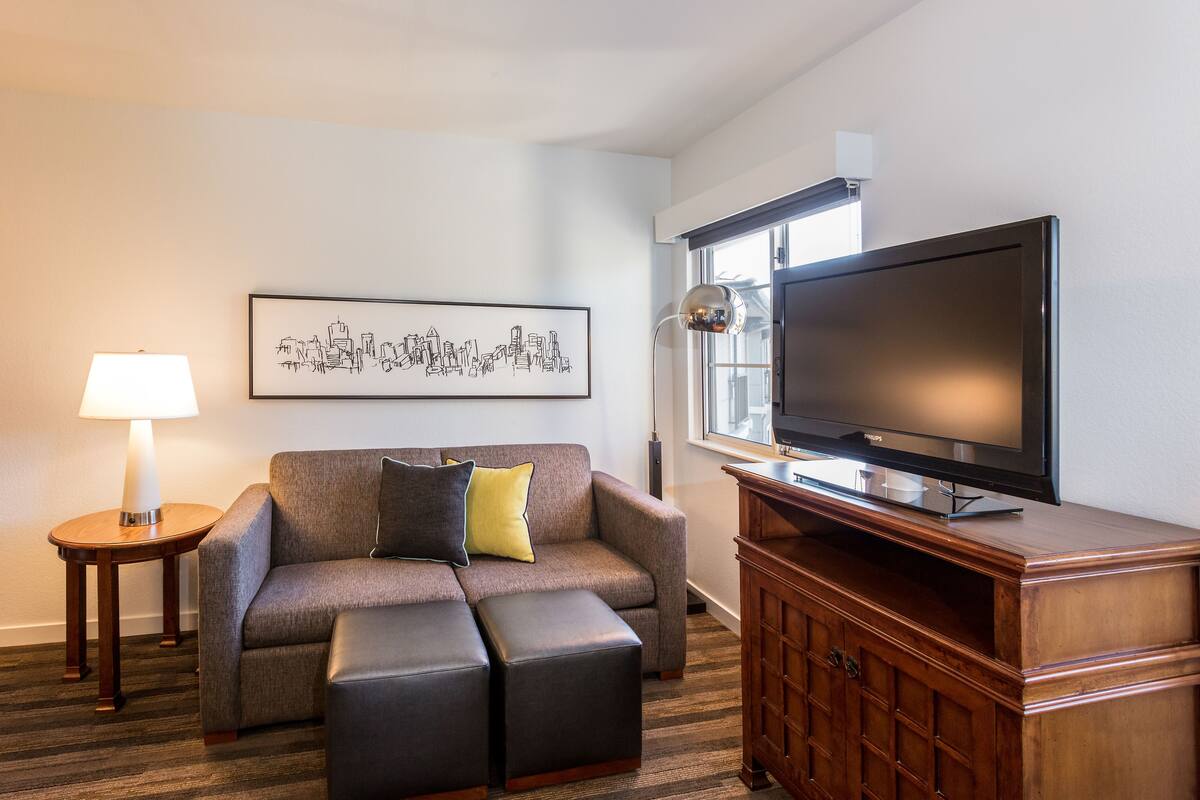 A modern living room with a grey sofa, a flat-screen TV, a wooden cabinet, and a framed cityscape artwork.