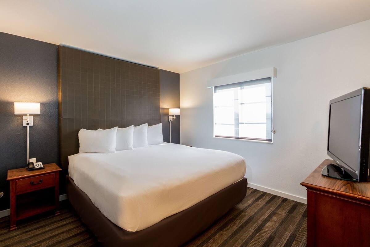 A hotel room with a large bed, bedside lamps, a television, and a window.