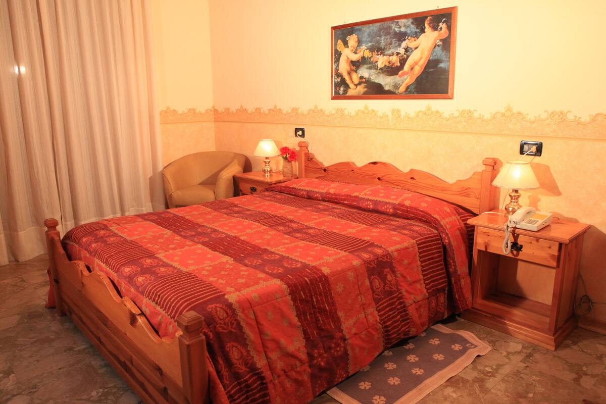 Een hotelkamer met een houten bed, twee nachtkastjes met lampen, een stoel en een schilderij aan de muur.