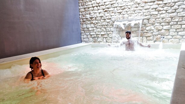 Zona de spa con pared de piedra y una bañera grande llena de agua.