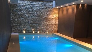 Una piscina con un muro de piedra de fondo e iluminación empotrada.