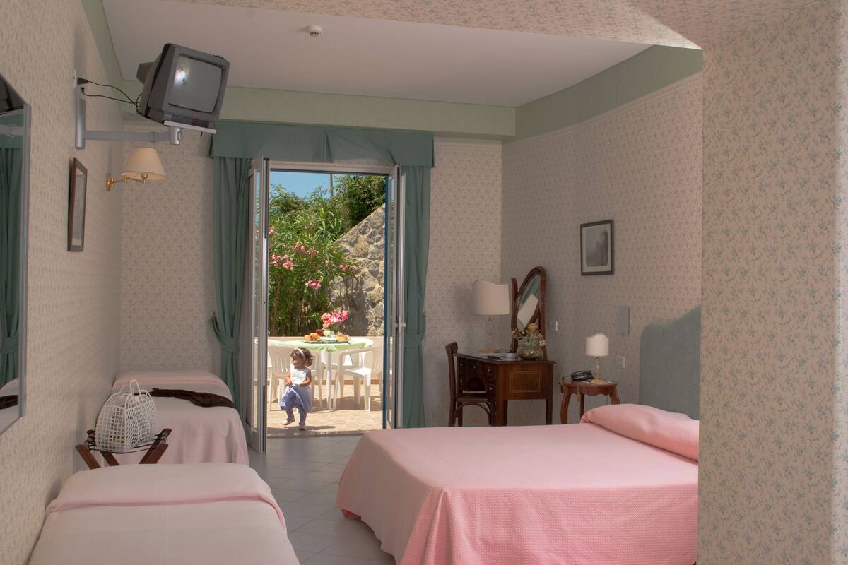 A hotel room with two beds, a television, a desk with a lamp, and a view of the outside.