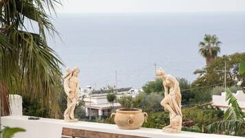 Un banco, dos estatuas, una planta en maceta y vista al mar.