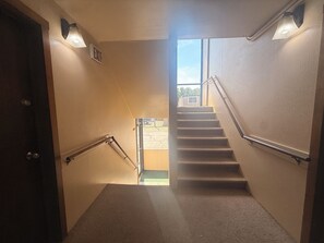 A carpeted stairway with handrails, an exit sign, and a view of the outside. - Autumn's Inn Roundup MT near Hwy 12 (Roundup)